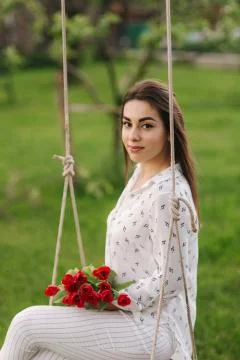 Lady in white sit on swing on the back yard of her house. She hold a re flowers Stock Photos