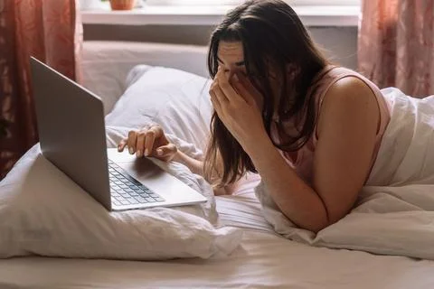 Lady working remotely while lying in bed with laptop Stock Photos