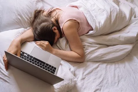 Lady working remotely while lying in bed with laptop Foto stock