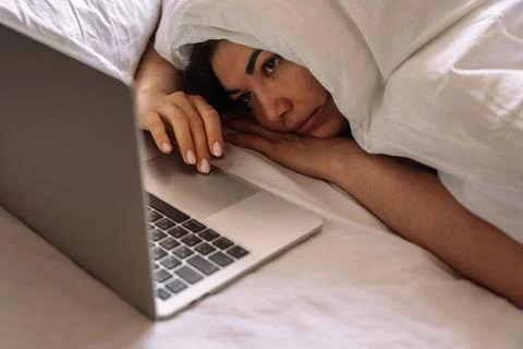 Lady working remotely while lying in bed talking on a video call Stock Photos