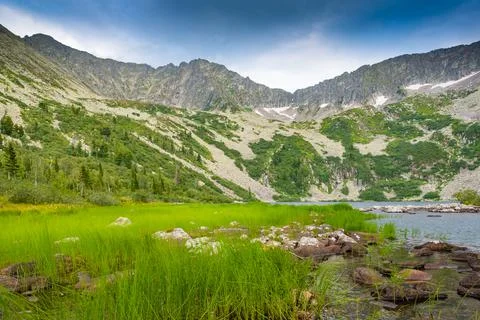 Lake at foot of mountain range. River in mountain valley along rocks. Summer  Stock Photos