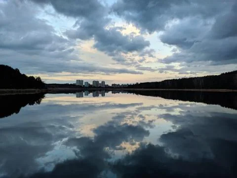 Lake in the forest, reflection of clouds in the water, houses on the horizon Фото