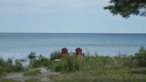 Lake Huron waterfront with red deck chairs and pine tree 库存影片 80191975