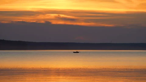 Lake. Man on boat rowing with oars silhouette. Orange sky reflects in water Stock Footage 224092860