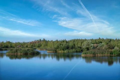 A lake with a plane surface and reflections against the blue sky. Stock Photos