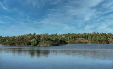A lake with a plane surface and reflections against the blue sky and white. Stock Photos