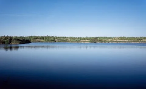 A lake with a plane surface and reflections against the blue sky and clouds. Stock Photos