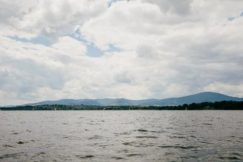 Lake reflecting cloudy sky with distant mountains and sailboats, offers serene Stock Photos