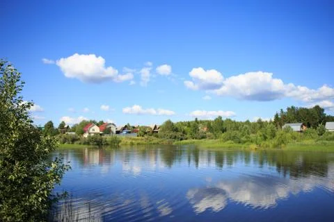 Lake reflecting sky with clouds on it flowing through a small village Stock Photos