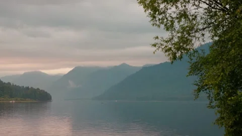 Lake shore at twilight. The sky is in the clouds, the mountains are in the Stock Footage 277532461