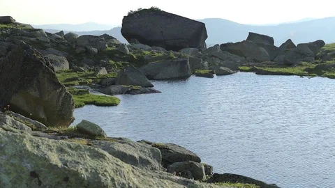 Lake surrounded by rocks against the backdrop of mountain ranges in the sun 스톡 동영상 78186384