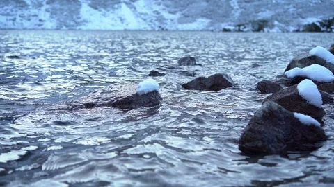 Lake surrounded by snow-capped mountains, stones covered with snow in water Stock-Footage 121366631
