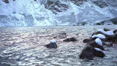 Lake surrounded by snow-capped mountains, stones covered with snow in water Video stock 121370706
