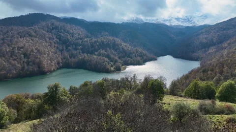 A lake surrounded by snow-capped mountains, green hills and thick clouds Video stock 310662648