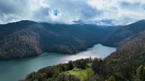 A lake surrounded by snow-capped mountains, green hills and thick clouds Stock Footage 310662890