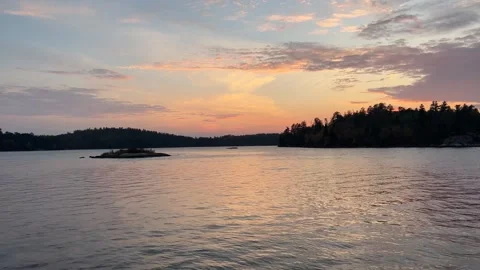 Lake water reflects a soft sunset near silhouetted forest Stock Footage 273176488