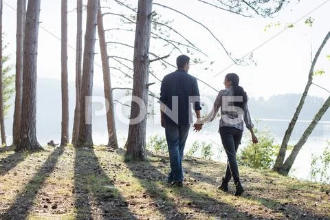 Lakeside. A Couple Walking In The Shade Of Pine Trees In Summer.