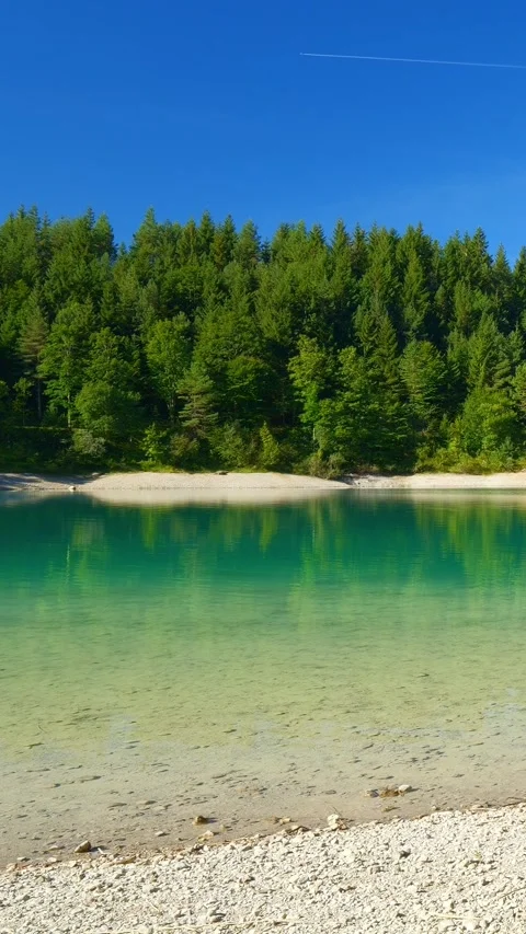 Lakeside view with deep blue glacial water, forested foothills, and jagged mo Stock Footage 308299736