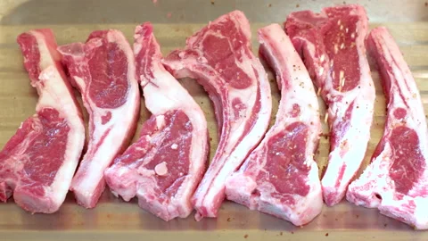 Lamb chops on wooden board being spiced and seasoned before barbecue Stock-Footage 331972243