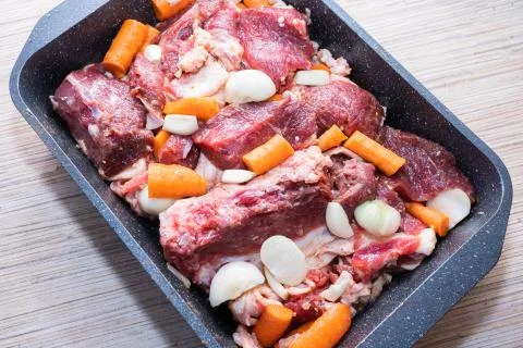 Lamb meat on a baking sheet marinated with spices, vegetable oil, carrots and Stock Photos