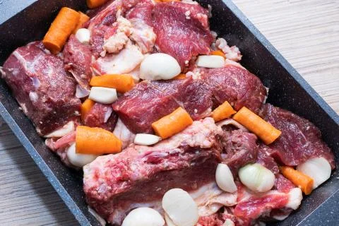 Lamb meat on a baking sheet marinated with spices, vegetable oil, carrots and Stock Photos