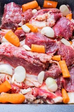 Lamb meat on a baking sheet marinated with spices, vegetable oil, carrots and Stock Photos