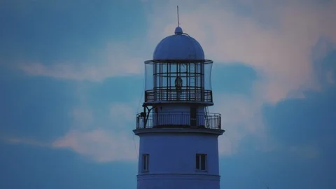 The lamp of a large white lighthouse shines with yellow light. Stockbeeldmateriaal 111894796