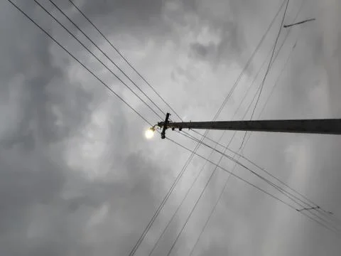 Lamp post with lighten bulb in cloudy weather and wires Stock Photos