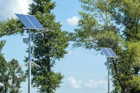 Lamp post with solar panel system on road with blue sky and trees. Autonomous Stock Photos