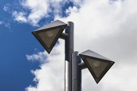 Lamp posts of a triangular shape against a blue cloudy sky. 스톡 사진
