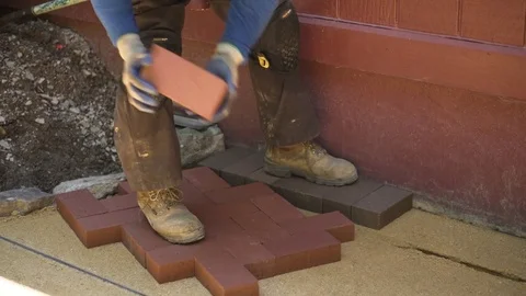 Landscape architect puts red brick pavers into a herringbone pattern as he Stock Footage 81559306