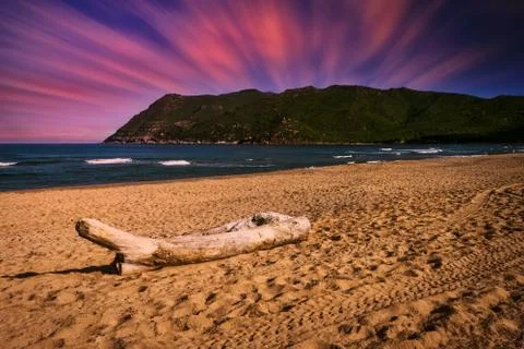 Landscape of beach at dramatic sunset with long exposure clouds and sky Stock Photos