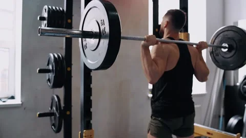 The landscape behind the bodybuilder performs barbell squats with weights on the Stock Footage 156866350
