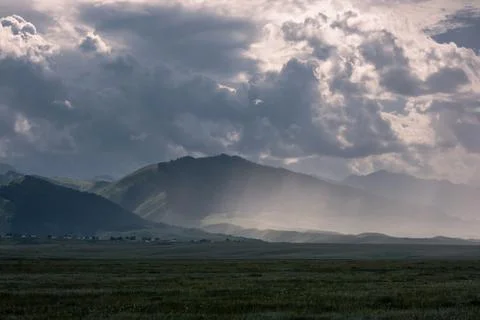 A landscape featuring cloud-covered mountains and a wide field in the foregro Stock Photos