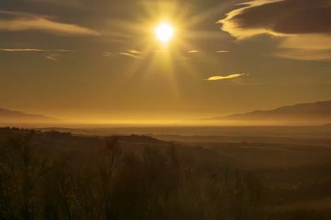 Landscape of fields and low mountains with mists, with a star-shaped sun givi Stock Photos