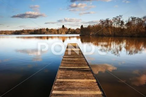 Landscape of fishing jetty on calm lake at sunset with reflections Stock Photos