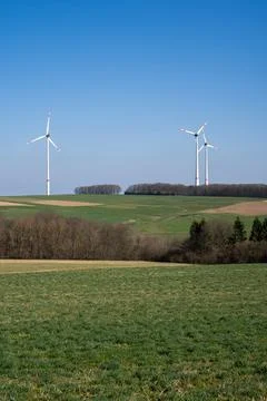 Landscape with grass, trees and wind turbines on a sunny day with blue sky Stock Photos