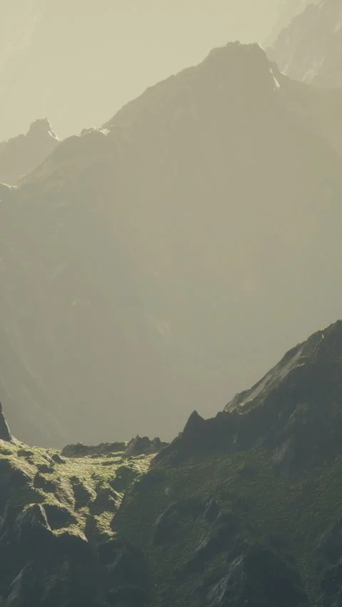 A landscape has steep mountains with rocky surfaces and patches of green grass Stock Footage 334884971