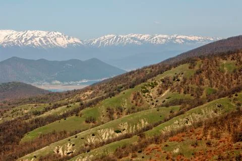 Landscape of a lake between spring hills and snow-covered mountain peaks. Stock Photos