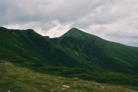 A landscape of a mountainous area covered with grass and stones. Cloudy mount Stock Photos
