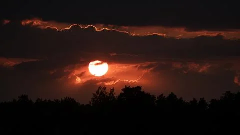 Landscape with red sun setting behind dark clouds Foto stock