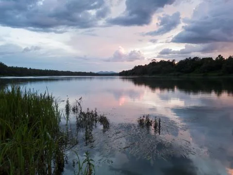 Landscape with river, clouds, water grass and mountain in distance at sunset. Stock Photos