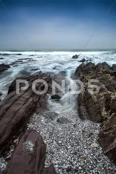 Landscape seascape of jagged and rugged rocks on coastline with long exposure Stock Photos