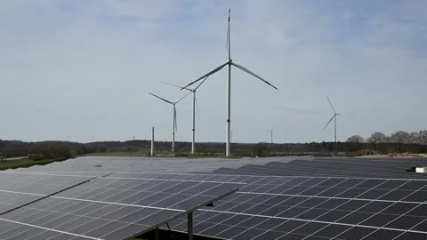 Landscape shot featuring a solar farm with rotating wind turbines behind it 動画素材 333805925