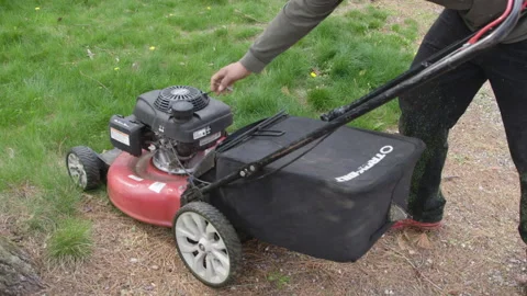 Landscaper attempts to start motor on small lawnmower with pull string Stock Footage 153311468