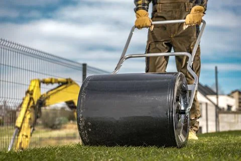 Landscaper Pushing Grass Roller to Compact New Turfs in a Backyard Garden 库存照片