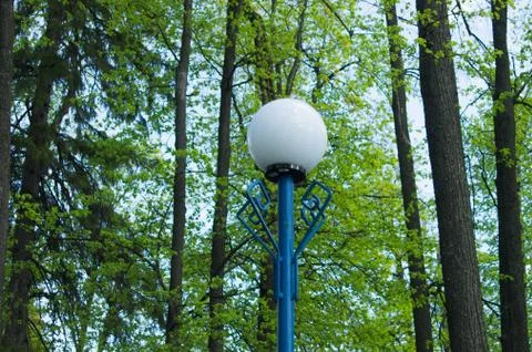 Lantern on a blue pillar between the trees in the park Stock Photos