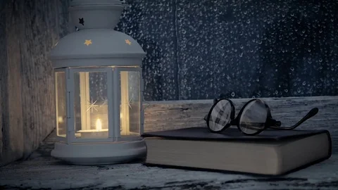 Lantern lit, book and glasses on the sill of an old window, it rains outside Stock Footage 74723635