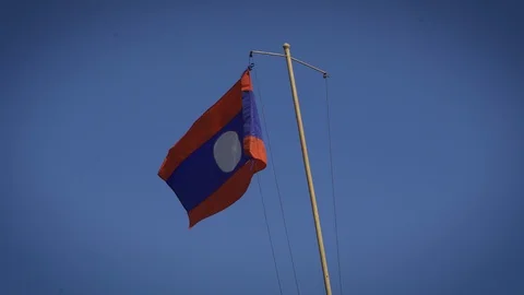 Lao Flag waving against clear blue sky with bird flying by Stock Footage 129490381