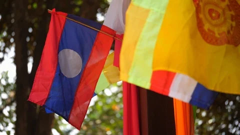Laos flag and buddhist prayer flags waving from the wind at Wat Phu Video stock 124396918